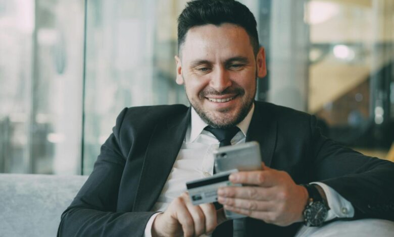 Man in suit smiling while holding phone and credit card